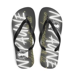 Overhead shot of black flip-flops with black toe straps. The words "Nopaune. Independent & Lit" are printed on both flip-flops in white and yellow. The letter O in "Nopaune" has been replaced with the Nopaune logo (a chess pawn with a "not allowed sign" laid over it, surrounded by spokes/rays and broken infinity signs).
